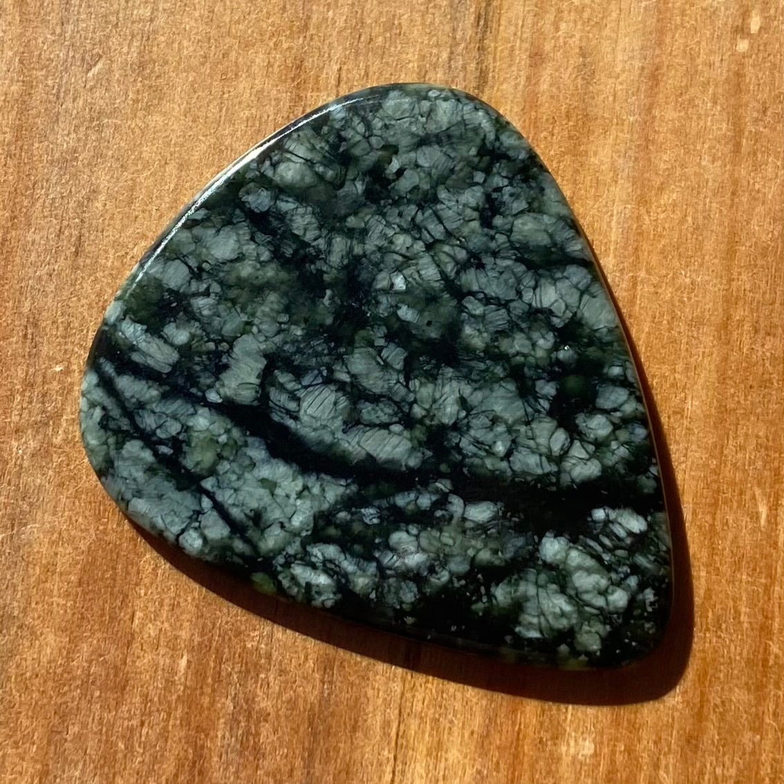 Guitar pick hand-carved from New Zealand tangiwai pounamu (greenstone). Front.