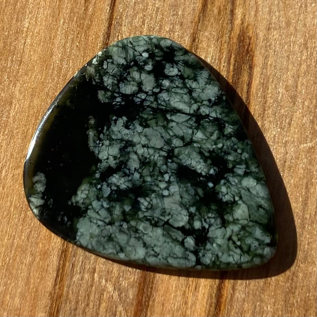 Guitar pick hand-carved from New Zealand tangiwai pounamu (greenstone). Front.