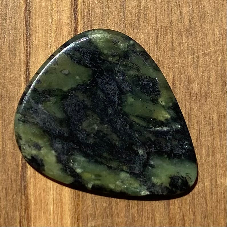 Guitar pick hand-carved from New Zealand Douglas Creek pounamu (greenstone). Back. 