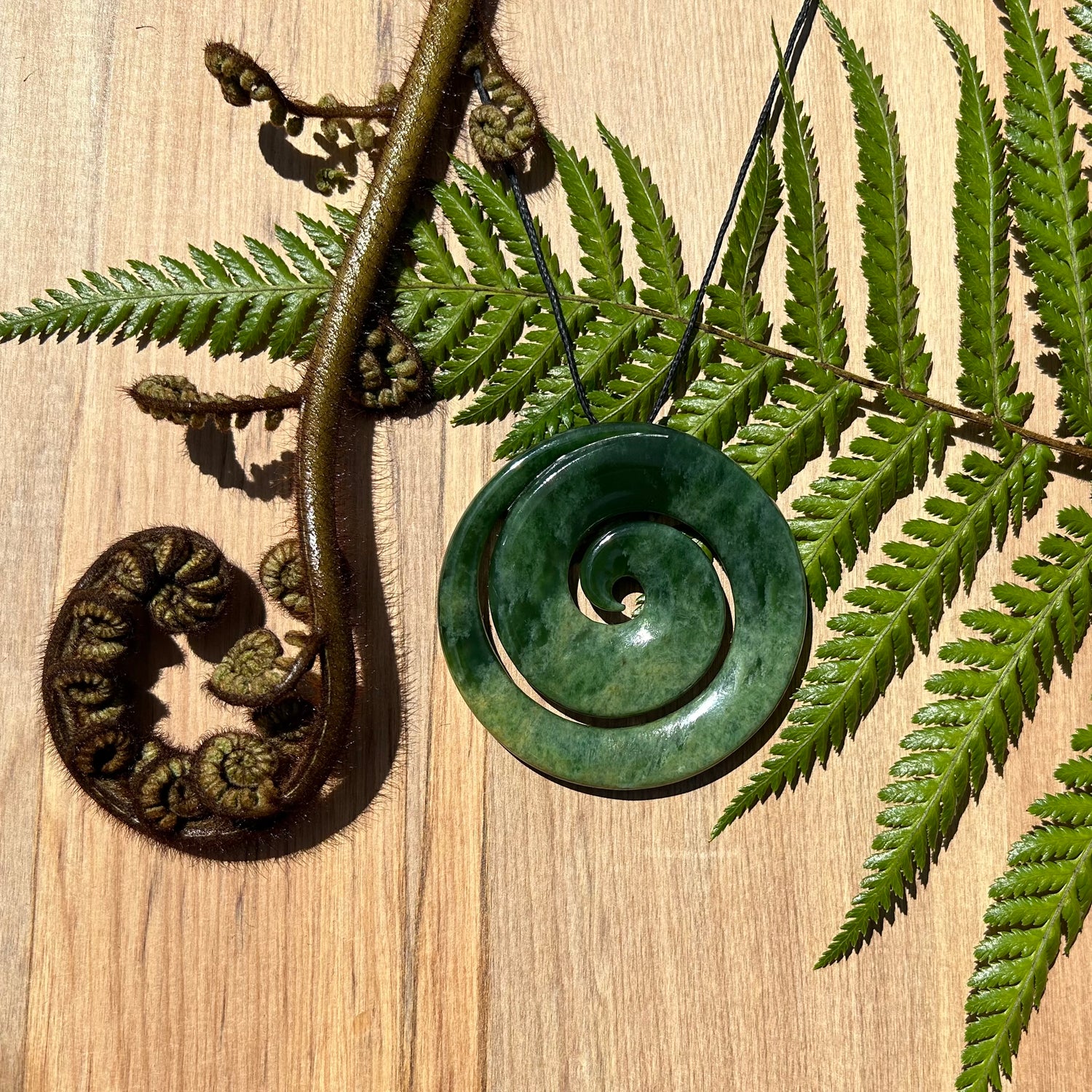 Koru pendant carved from NZ jade pounamu alongside fern frond