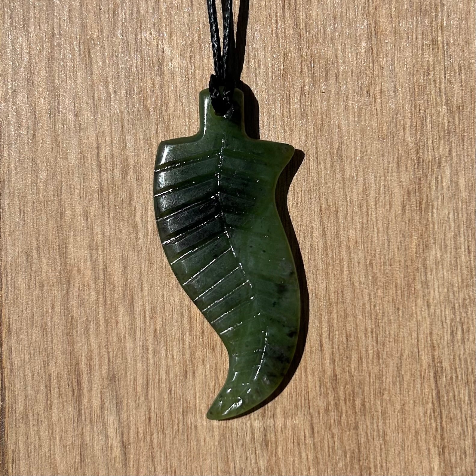 Fern pendant hand-carved from New Zealand kawawkawa pounamu (greenstone). Front.