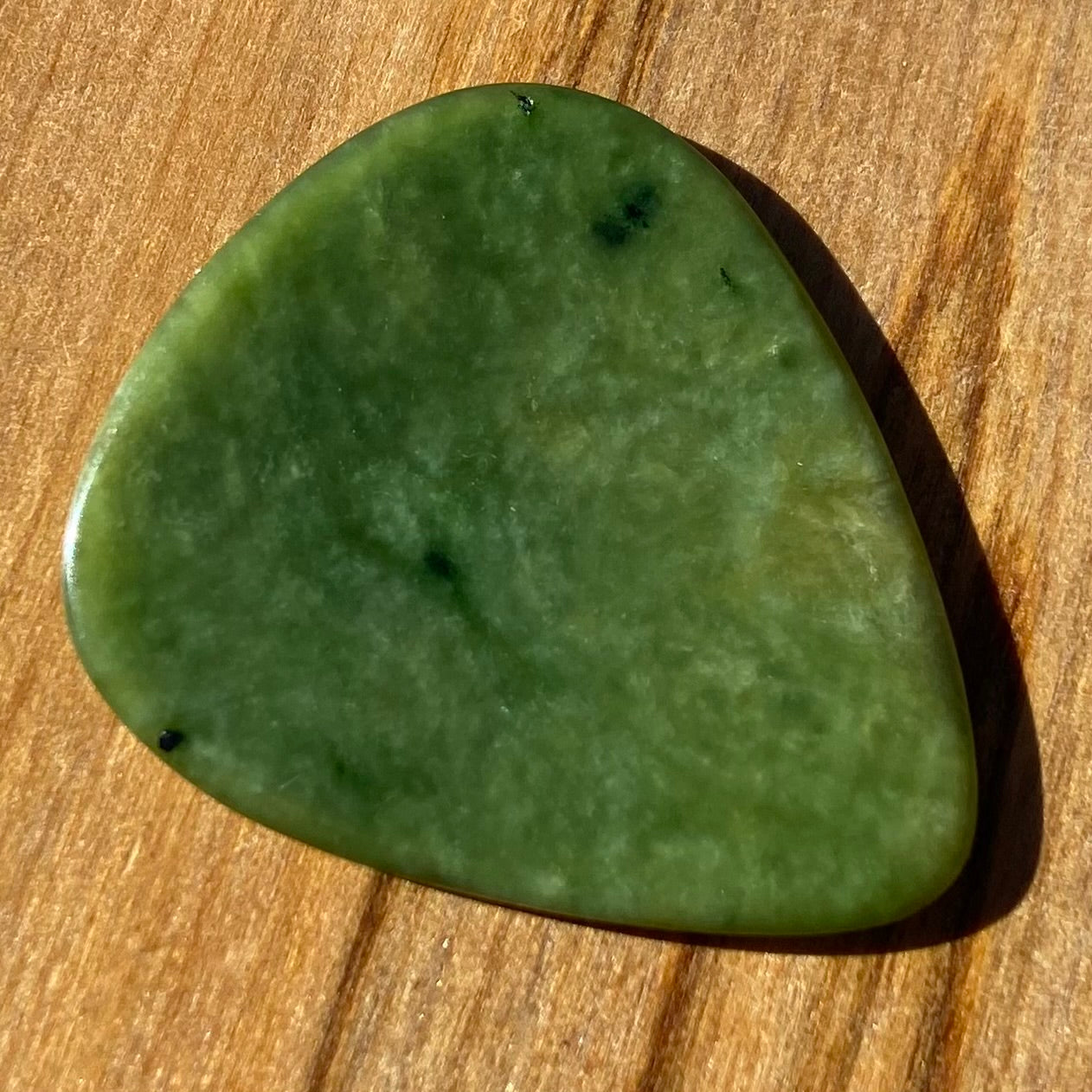 Pounamu guitar pick hand-carved from New Zealand Marsden flower jade pounamu (greenstone). Front.