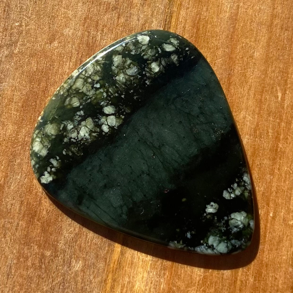 Guitar pick hand-carved from New Zealand tangiwai pounamu (greenstone). Front.