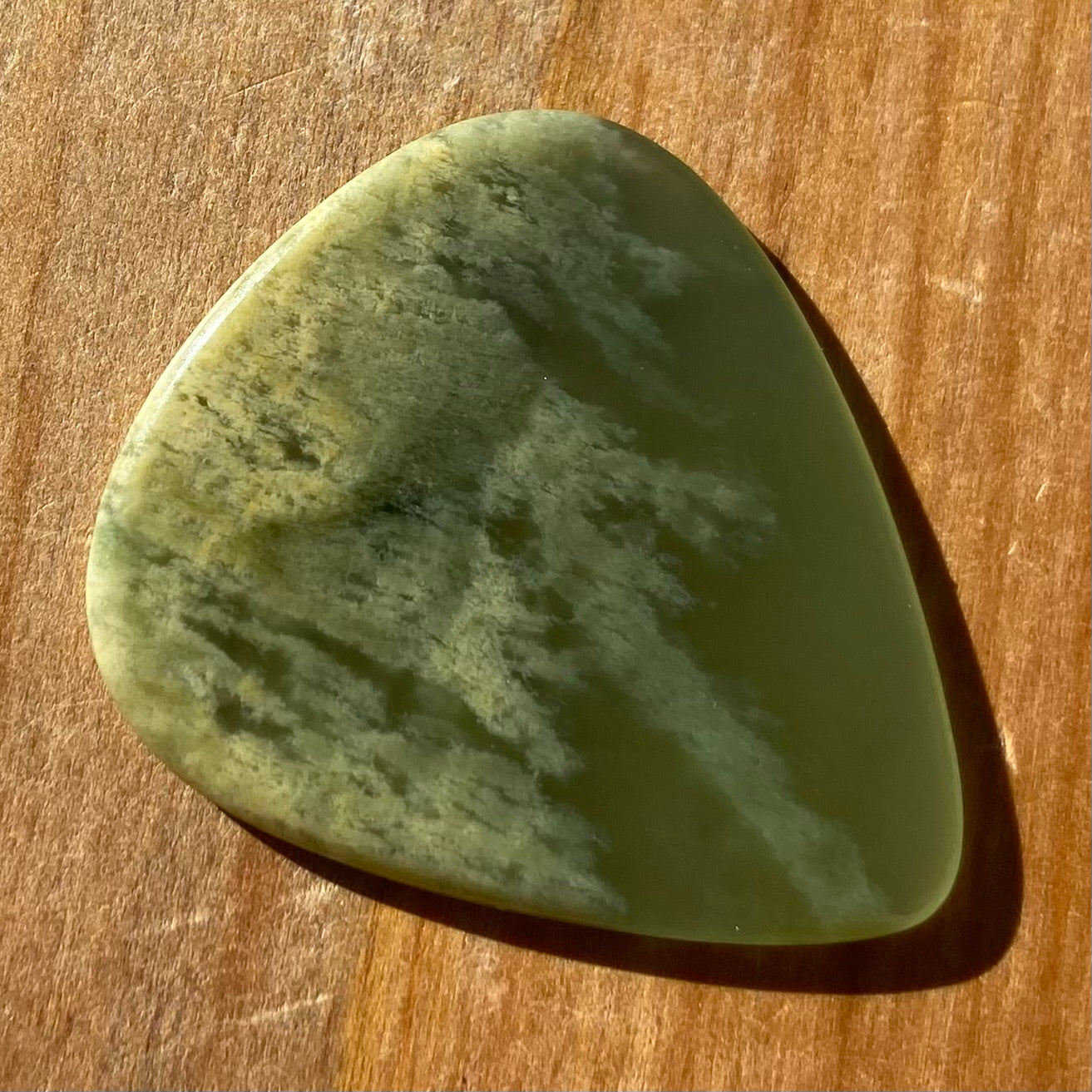 Pounamu guitar pick hand-carved from New Zealand Marsden flower jade pounamu (greenstone). Front.