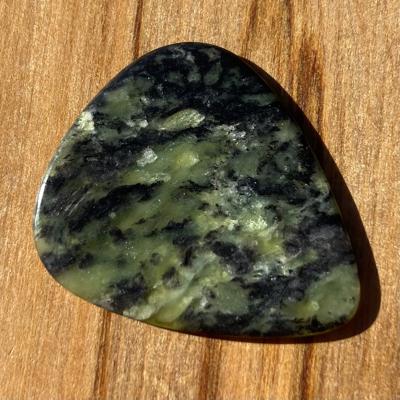 Guitar pick hand-carved from New Zealand Douglas Creek pounamu (greenstone). Front.