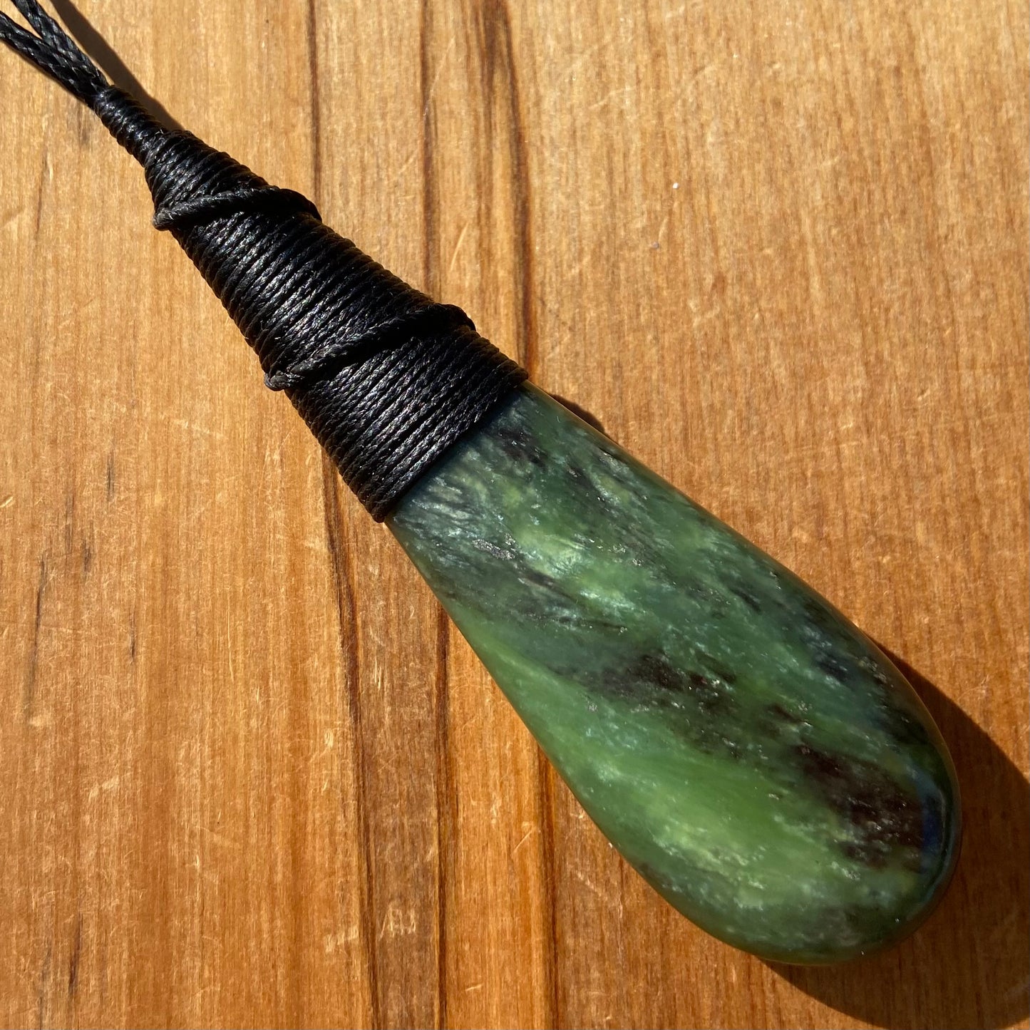 Bound roimata (teardrop) pendant hand-carved from New Zealand Kawakawa pounamu (greenstone). Front.