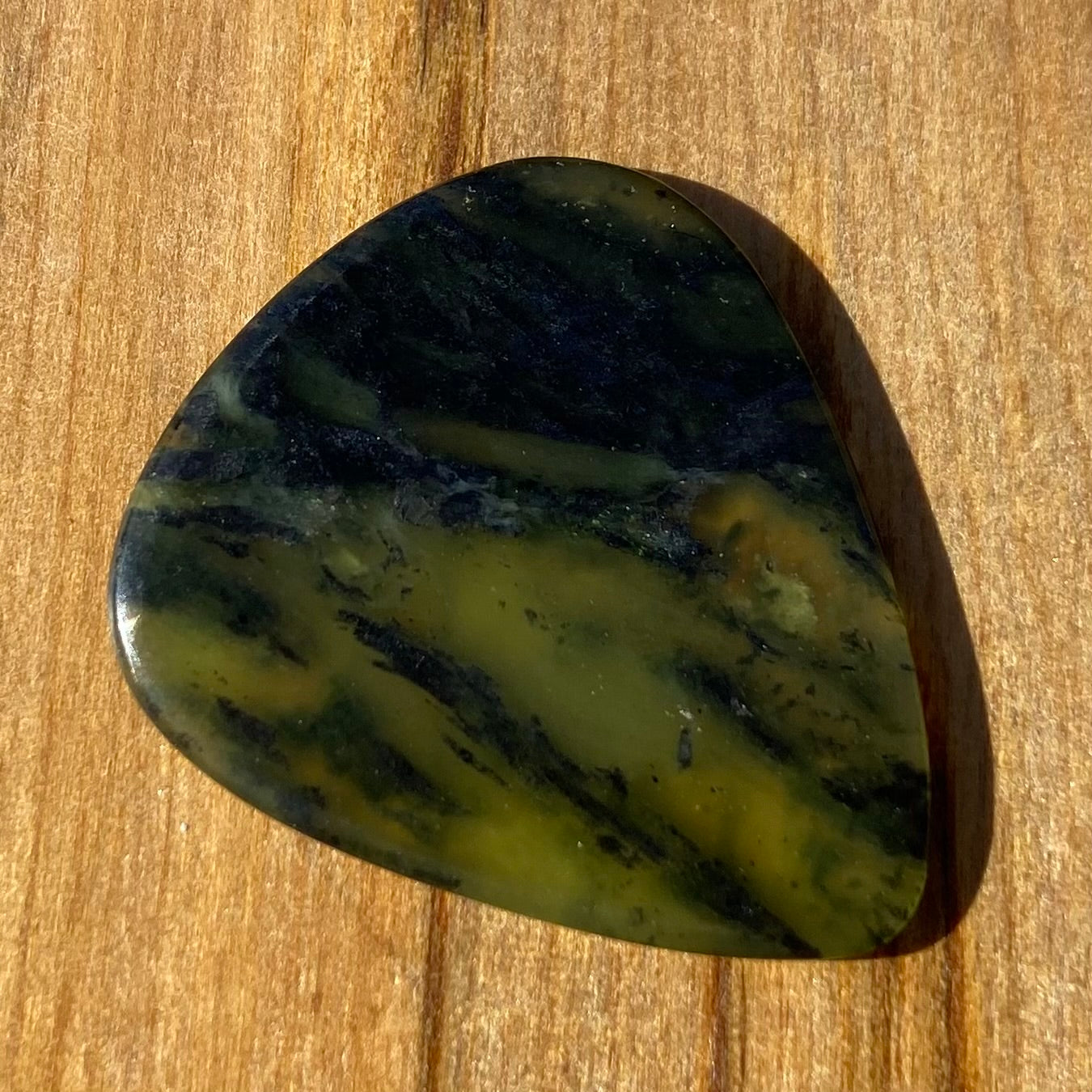 Guitar pick hand-carved from New Zealand Douglas Creek pounamu (greenstone). Front.