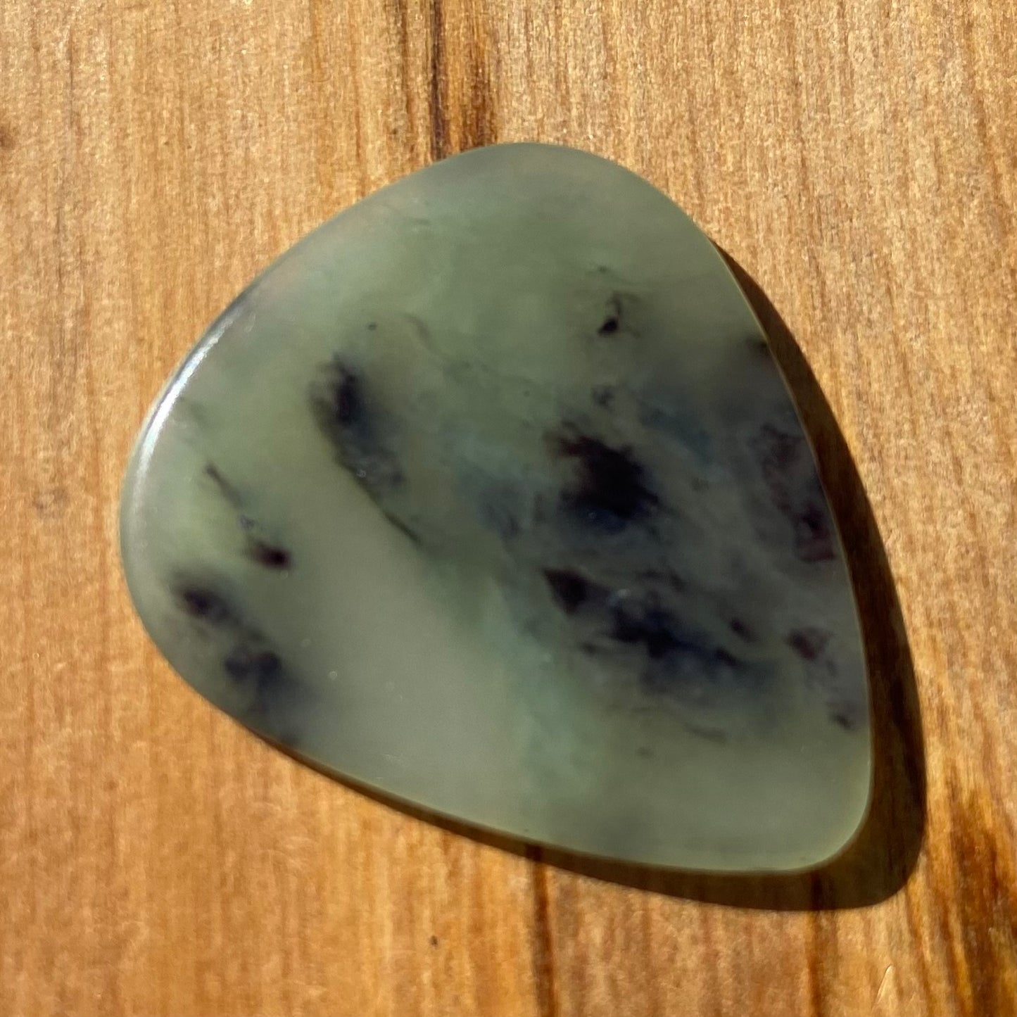 Guitar pick hand-carved from New Zealand Inanga Greenstone pounamu (greenstone). Front.