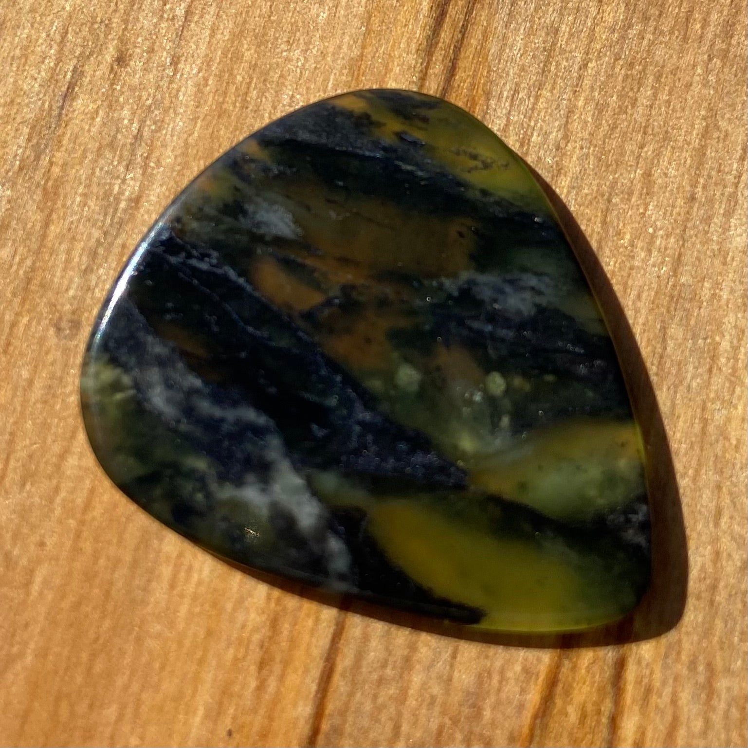 Guitar pick hand-carved from New Zealand Douglas Creek pounamu (greenstone). Front.