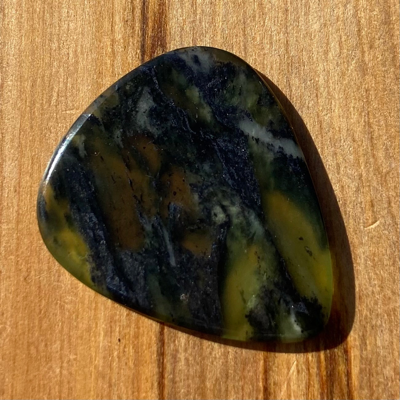 Guitar pick hand-carved from New Zealand Douglas Creek pounamu (greenstone). Front.