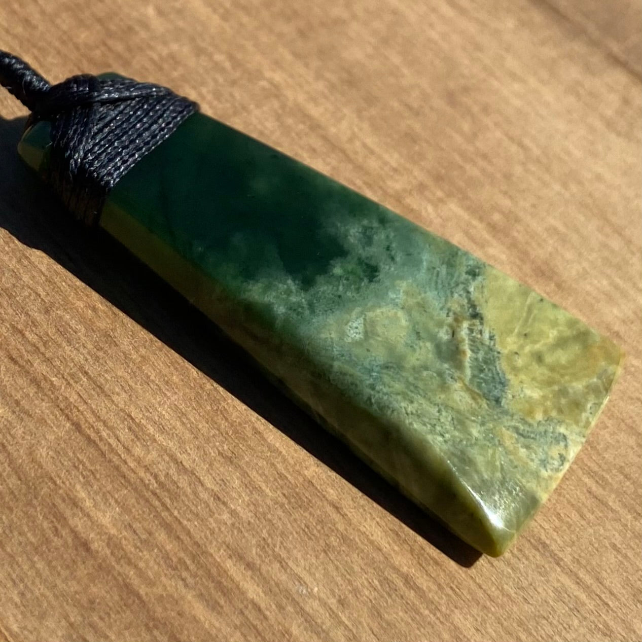 Bound toki pendant hand-carved from New Zealand Marsden Flower Jade pounamu (greenstone). Angle.