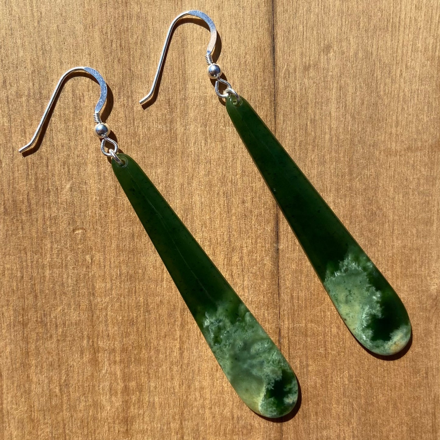 Pair of roimata (teardrop) earrings hand-carved from New Zealand Marsden Flower Jade/ pounamu (greenstone), with sterling silver fittings. Front.