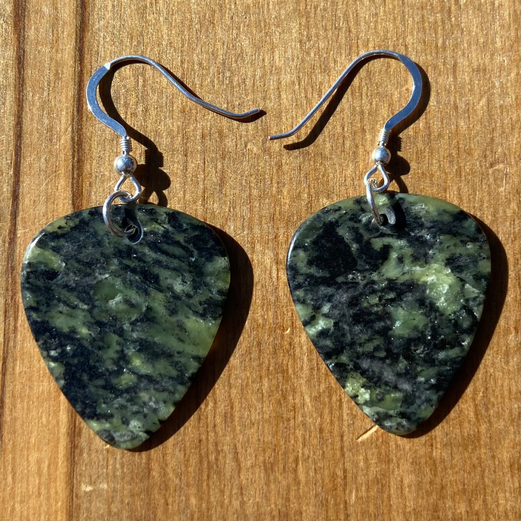 Guitar pick earrings hand-carved from New Zealand Douglas Creek pounamu (greenstone) fitted with sterling silver. Front.