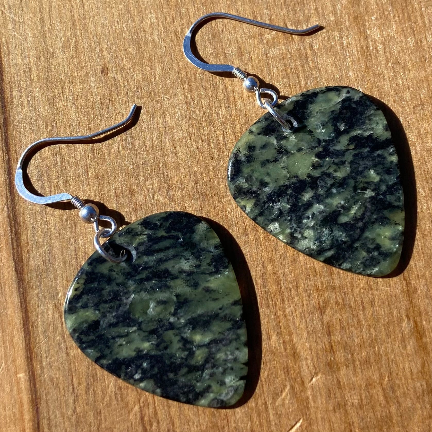 Guitar pick earrings hand-carved from New Zealand Douglas Creek pounamu (greenstone) fitted with sterling silver. Front.