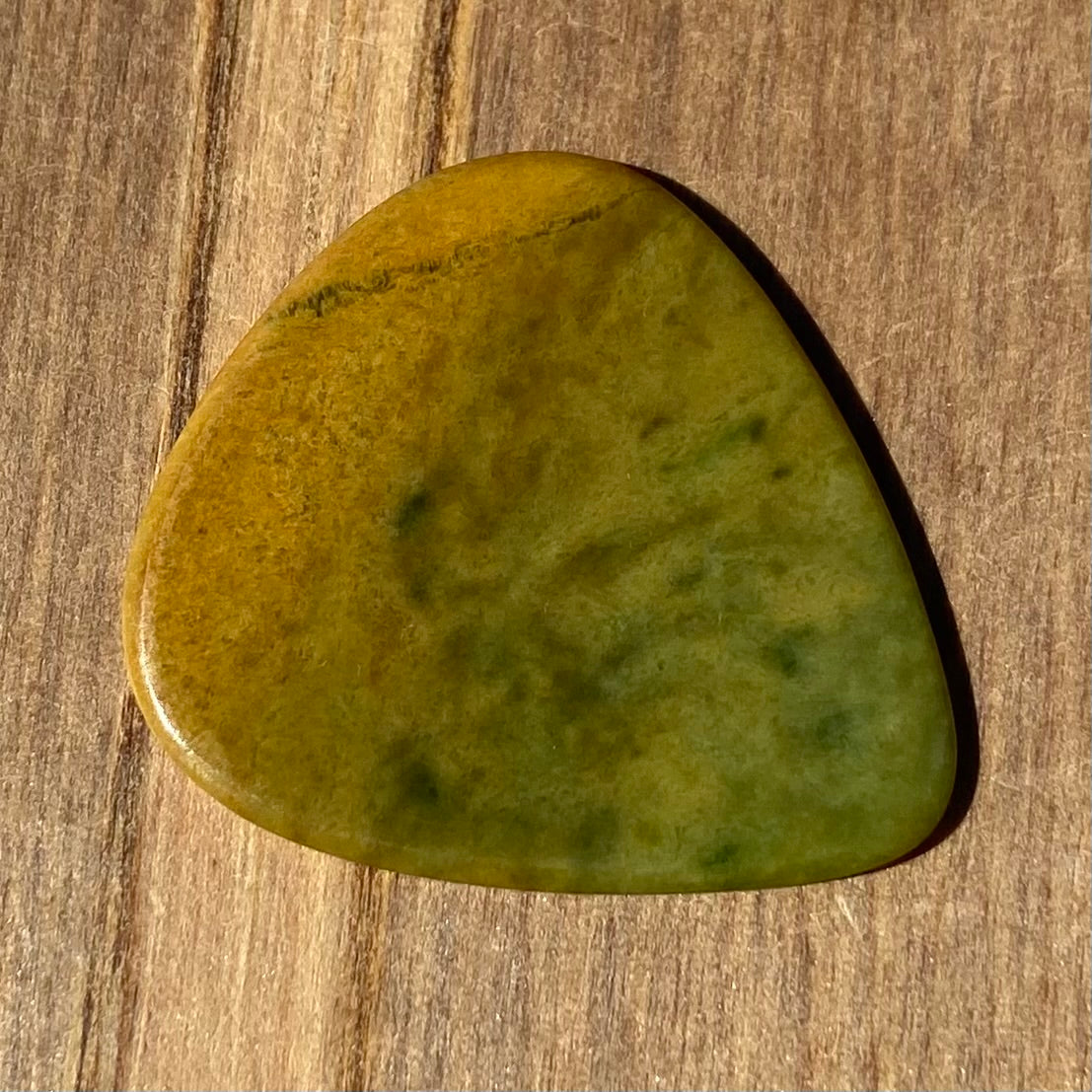 Guitar pick hand-carved from New Zealand Marsden flower jade pounamu (greenstone). Front.