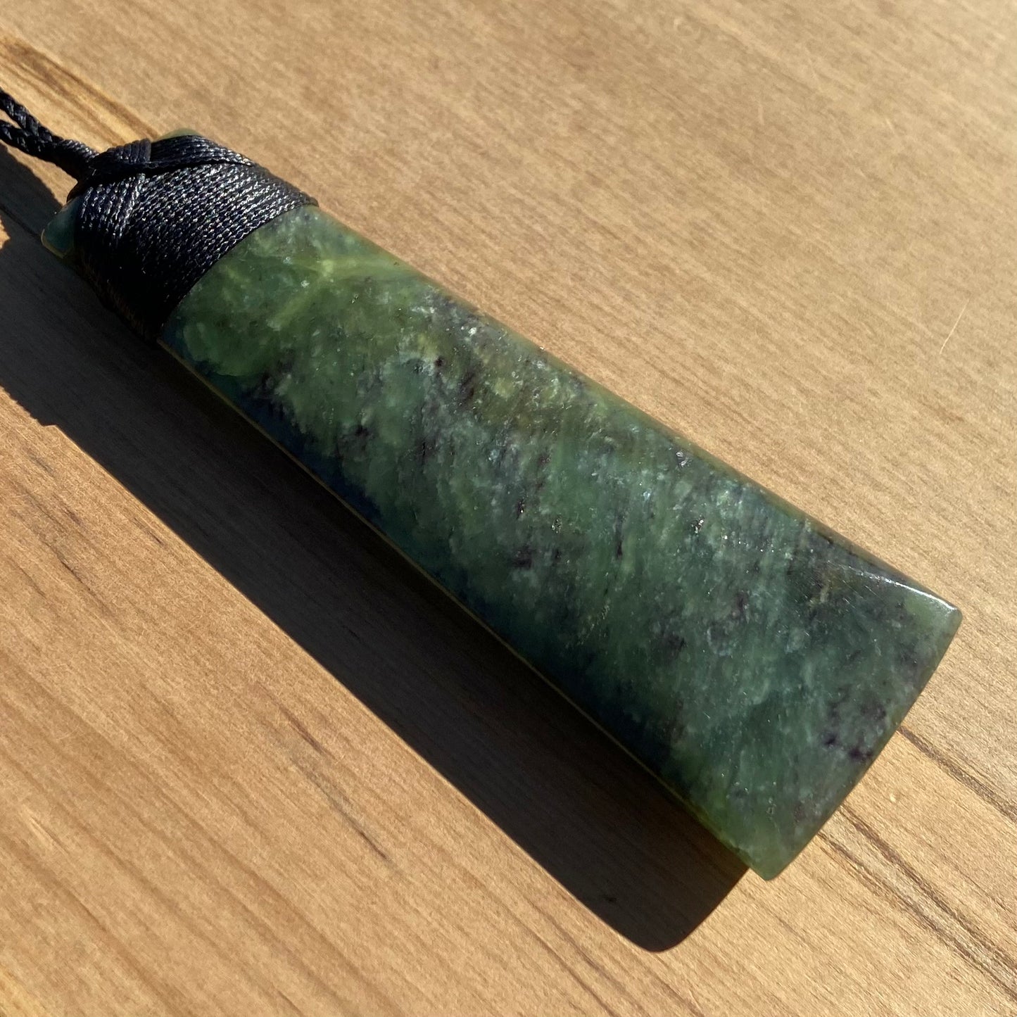 Bound toki pendant hand-carved from New Zealand totoweka pounamu (greenstone). Front angle.